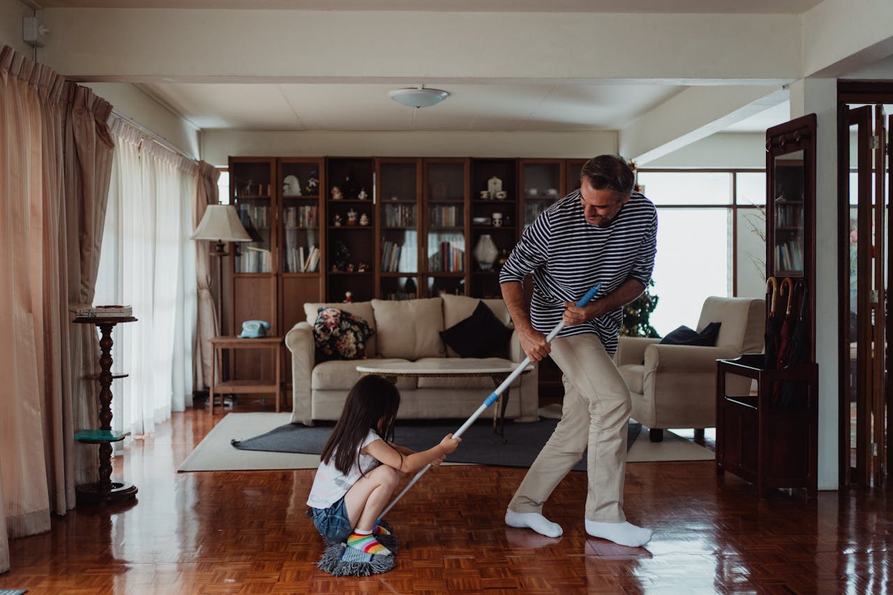 A playful moment as a father and daughter clean their living room, enhancing family bonding through chores.