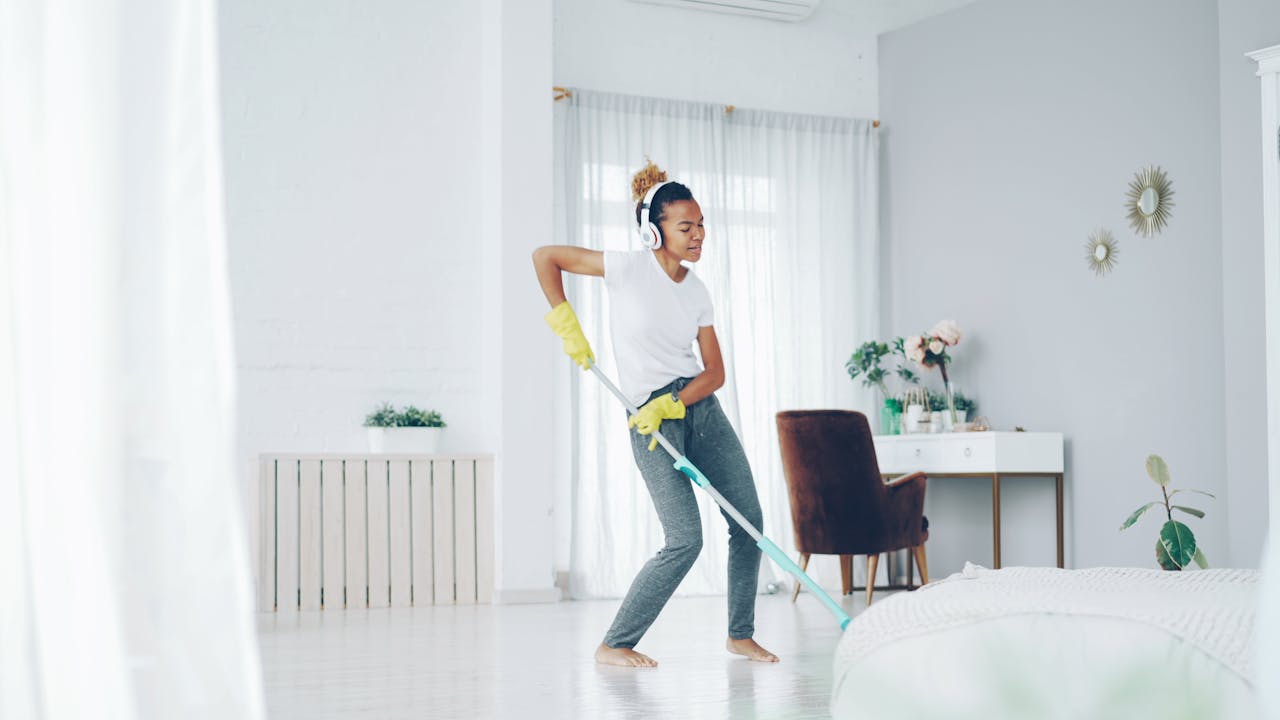 Cheerful young woman dances while mopping her bright, modern living room.