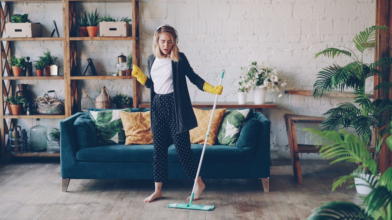 Woman cleaning living room with a mop at home, enjoying music.