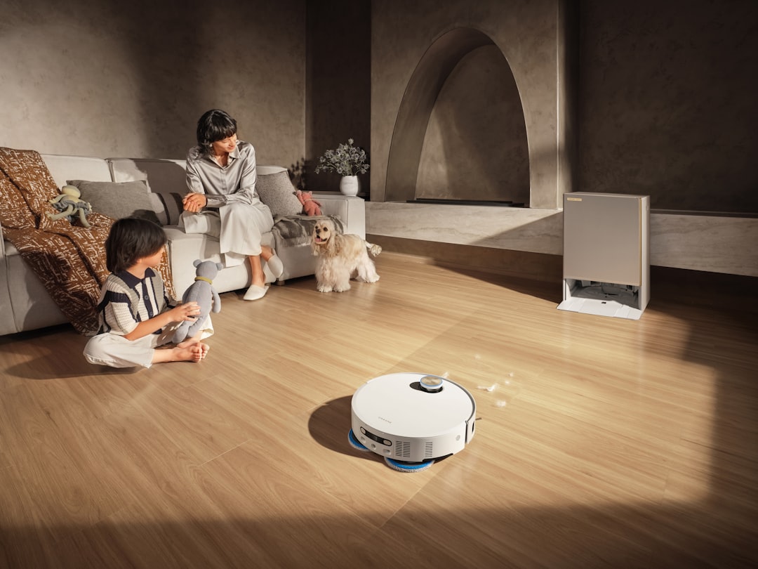 A Dreame robot vacuum and mop cleans the floor as a mother and child sit on the sofa with their pet, enjoying a cozy family moment.
